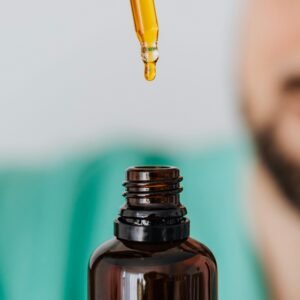 A dropper with golden oil suspended above an open amber bottle, close-up view.